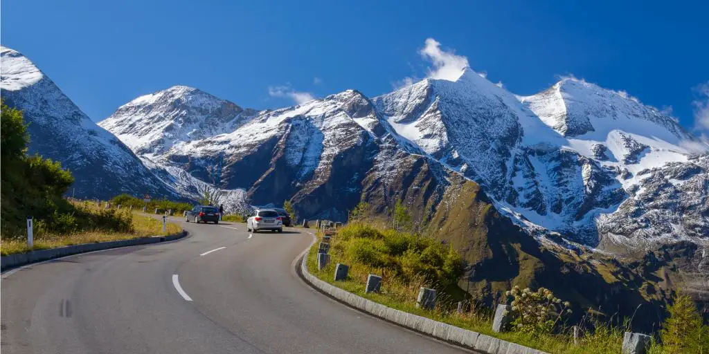 Un coche circulando por la carretera alpina de Grossglockner, Austria, con picos nevados en la distancia 