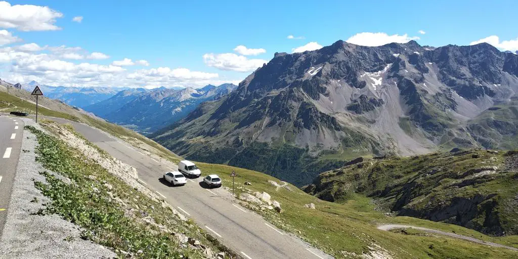 Coches aparcados a un lado de la carretera en el Col de la Bonette, Francia, con picos montañosos al fondo 