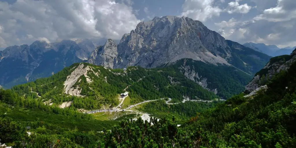 Vrsic Pass, Eslovenia camino a través de una colina verde con una montaña rocosa en el fondo 