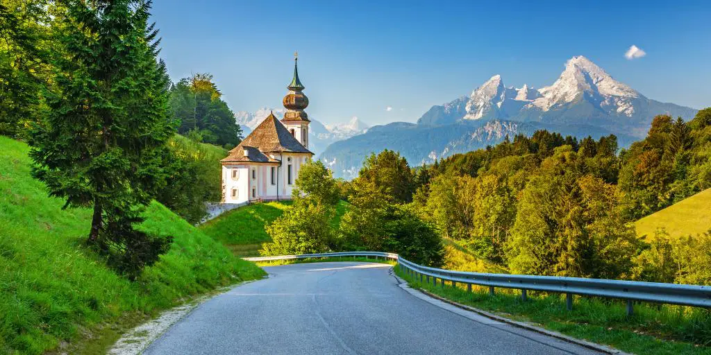 Una carretera con montañas, una iglesia y árboles al fondo en los Alpes bávaros