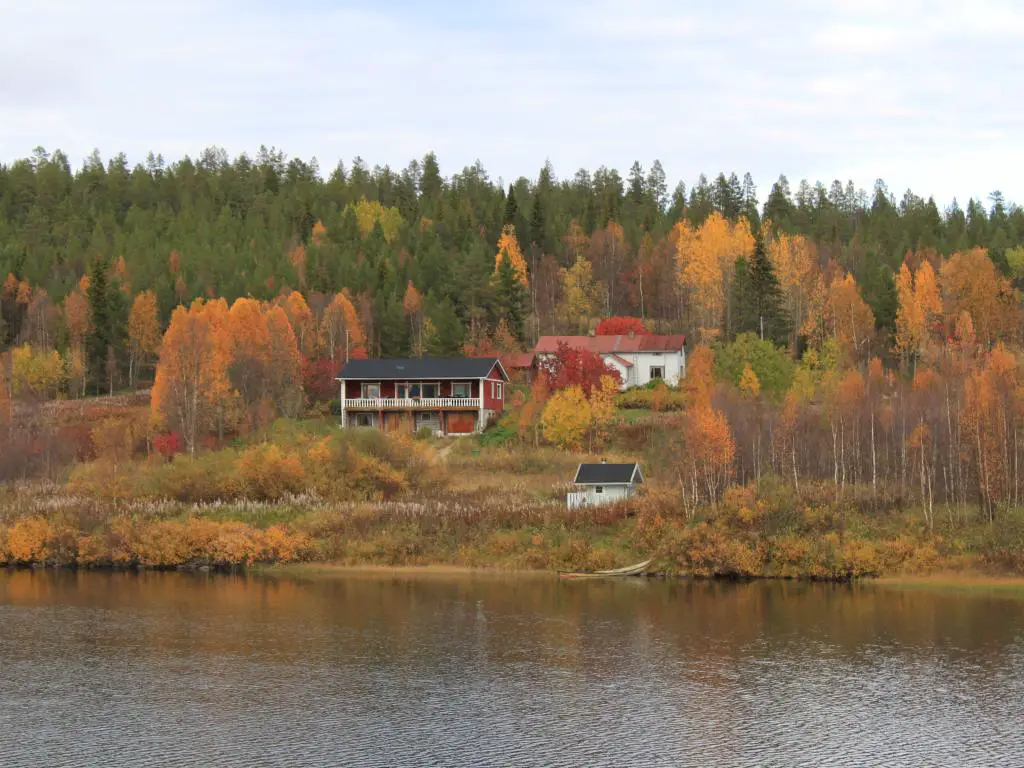 Una cabaña en un lago en un día de otoño está rodeada de coloridos árboles y árboles de hoja perenne.