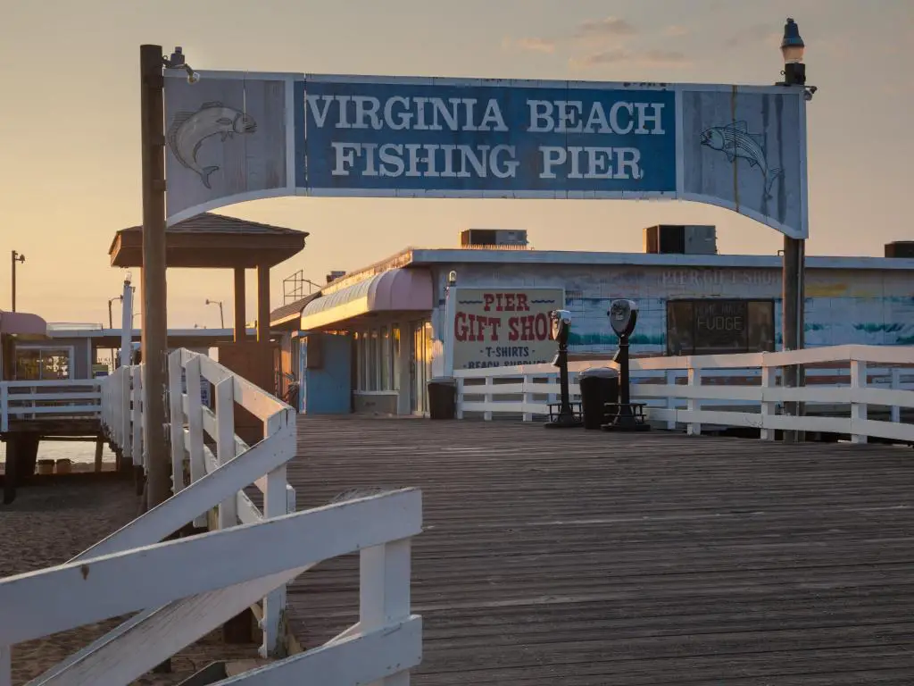 Entrada en arco señalizada al muelle de pesca de Virginia Beach al atardecer, con un cartel de una tienda de regalos en el fondo