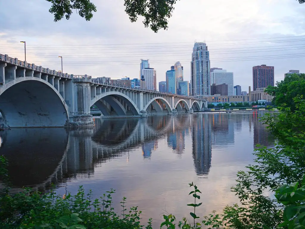 Minneapolis, Minnesota, EE.UU. con una vista de la ciudad de Minneapolis en una noche con un puente que cruza el río en primer plano.