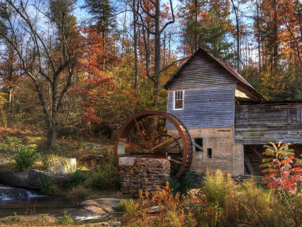 Un antiguo molino de madera en el bosque de Georgia, EE.UU., con hojas de otoño que se vuelven rojas y naranjas