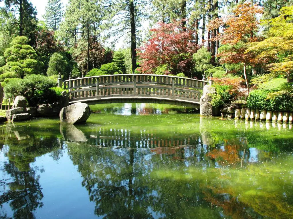 Puente de piedra adornado que cruza un pequeño cuerpo de agua con follaje otoñal reflejado en un lago tranquilo 