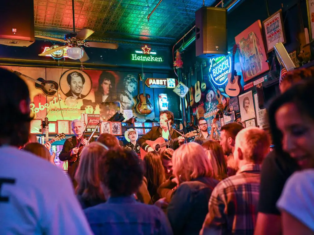 Un bar concurrido en el centro de Nashville, con gente viendo música en vivo.  Letreros de neón y recuerdos musicales se alinean en las paredes.