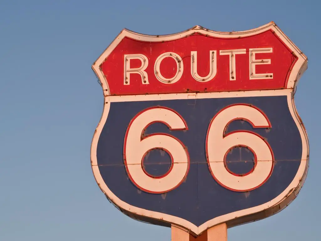 Letrero de neón rojo, blanco y azul de la ruta 66 en forma de escudo de la autopista estadounidense que brilla sin el neón al atardecer