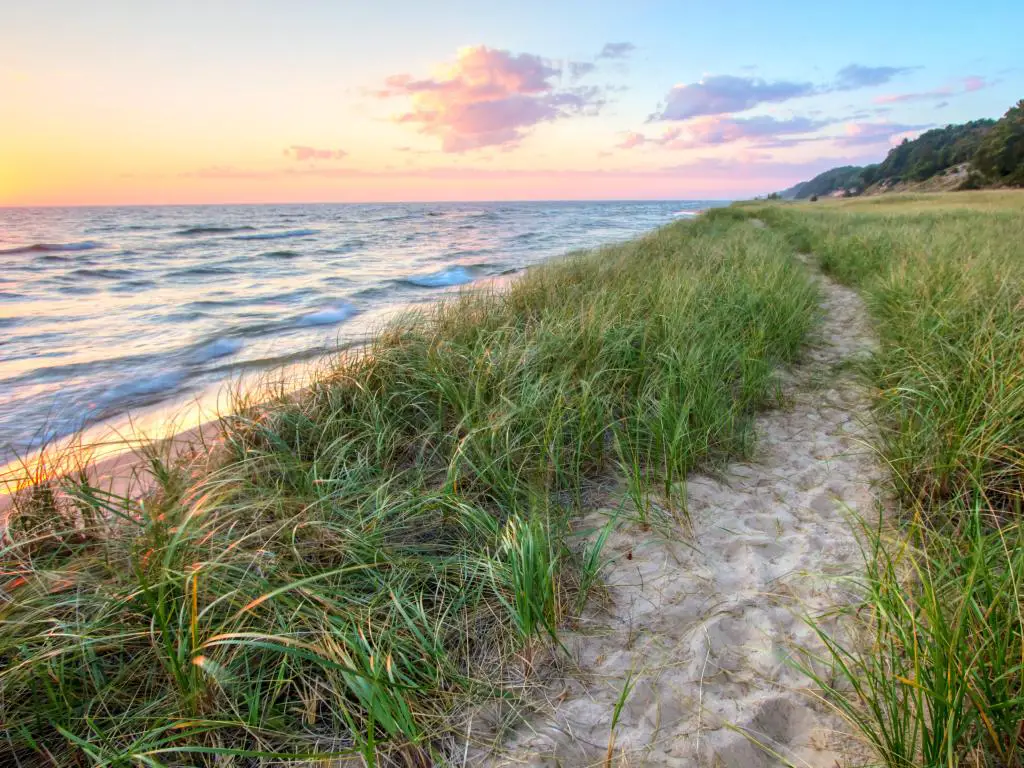 Lago Michigan, EE. UU. Con una playa y un camino de arena que serpentea a lo largo de la orilla del lago Michigan con un horizonte de puesta de sol y dunas de arena como telón de fondo. 
