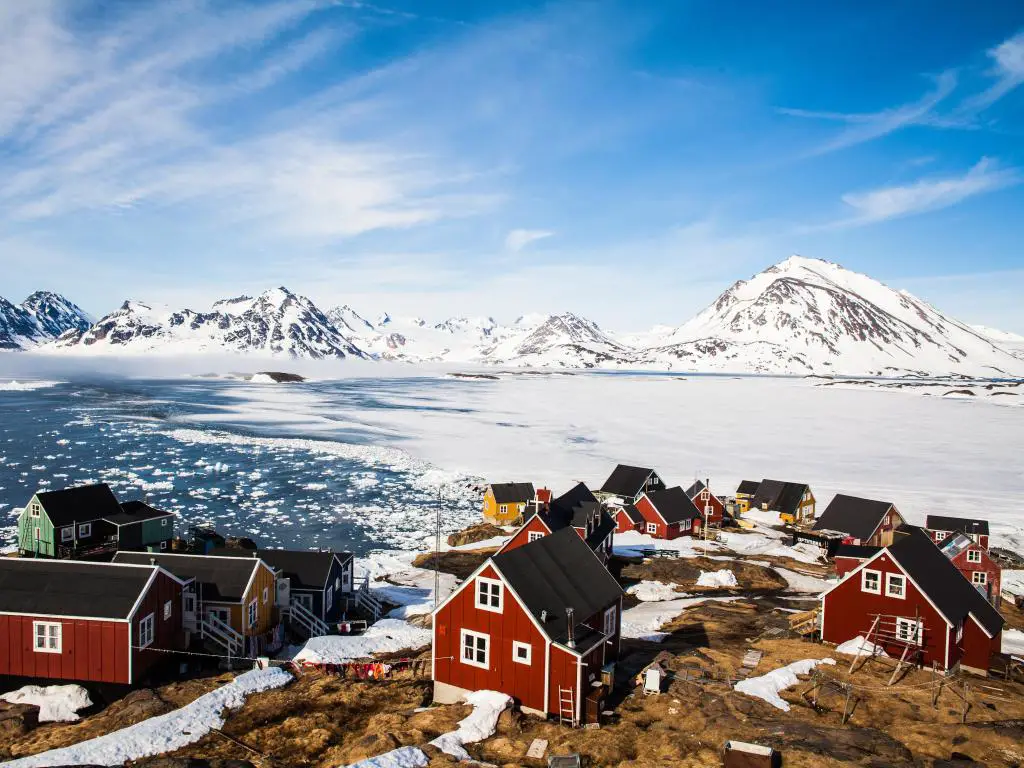 Pueblo típico de Groenlandia en la costa con montañas cubiertas de hielo al fondo.