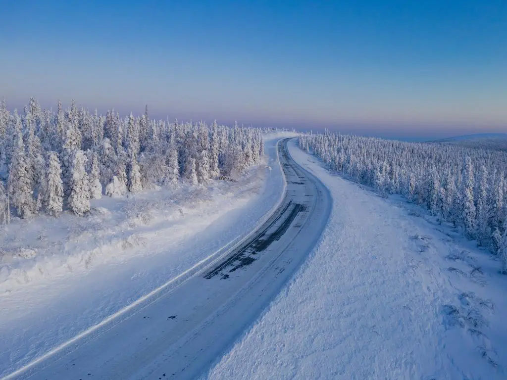 La carretera de hielo de Dalton Highway en medio del invierno pasando por un bosque de coníferas en el norte de Alaska.