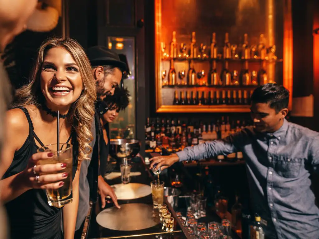 Un grupo de amigos pidiendo bebidas en un bar con el camarero trabajando duro