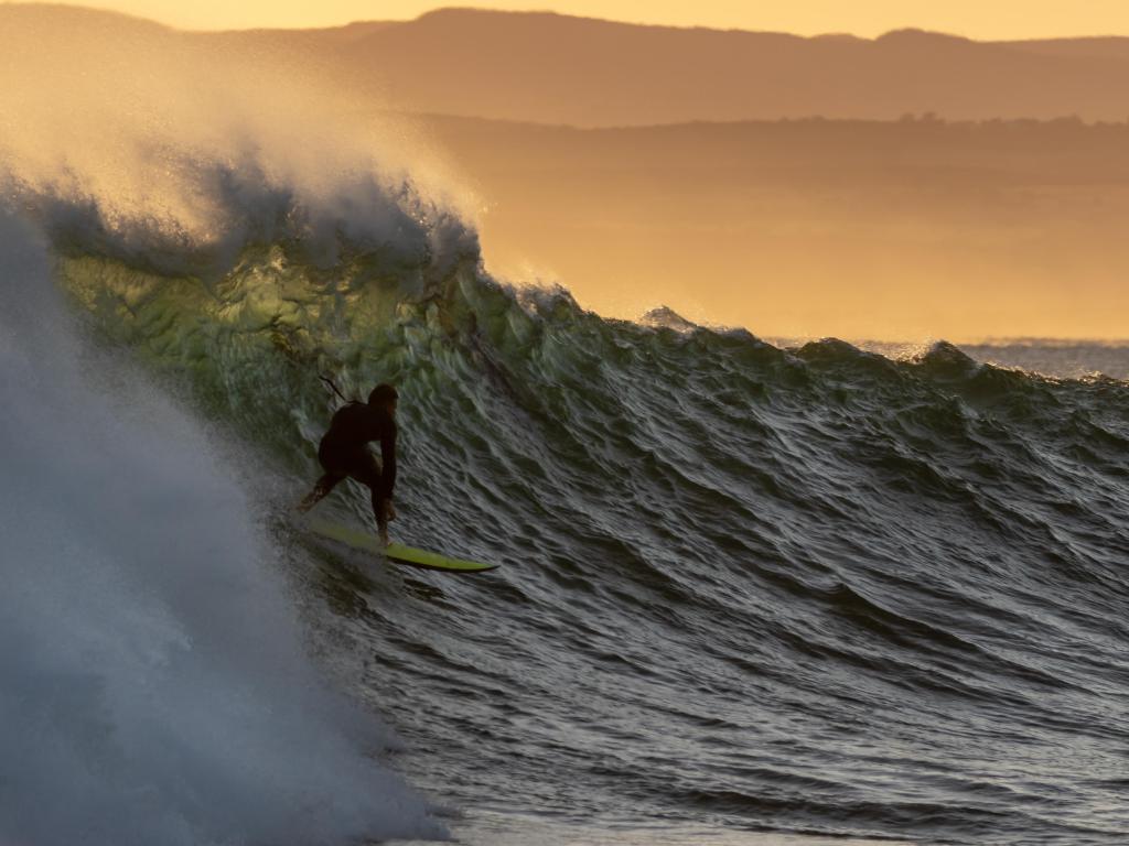 La silueta de un surfista al amanecer montando una ola en Jeffreys Bay en Sudáfrica