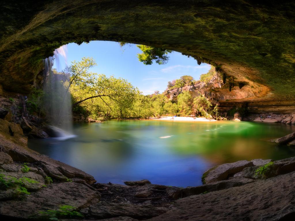 Hamilton Pool, Texas, EE. UU. con vista a una cascada, agua turquesa, playa y árboles con rocas que enmarcan la foto.
