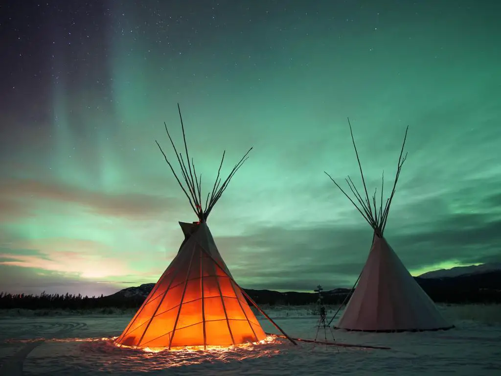 Tipis en Whitehorse, Yukón, Canadá, brillando desde dentro bajo un cielo nocturno con auroras boreales