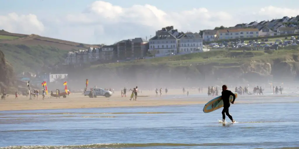 Persona que practica surf corre a través de una playa en Cornualles