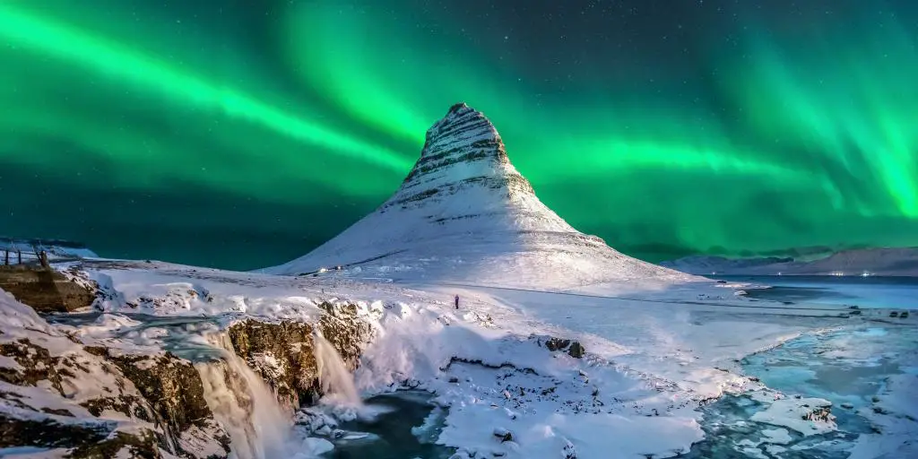 Auroras boreales verdes en el cielo de Islandia, con una montaña cubierta de nieve y cascadas debajo