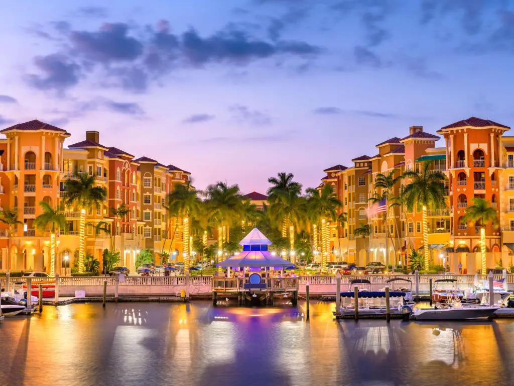 Skyline del centro de Naples, Florida al atardecer.  Los botes pequeños están amarrados en el muelle frente a palmeras brillantemente iluminadas.
