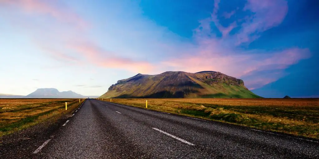 Mirando hacia abajo por una carretera con una montaña a un lado durante una colorida puesta de sol, en Islandia