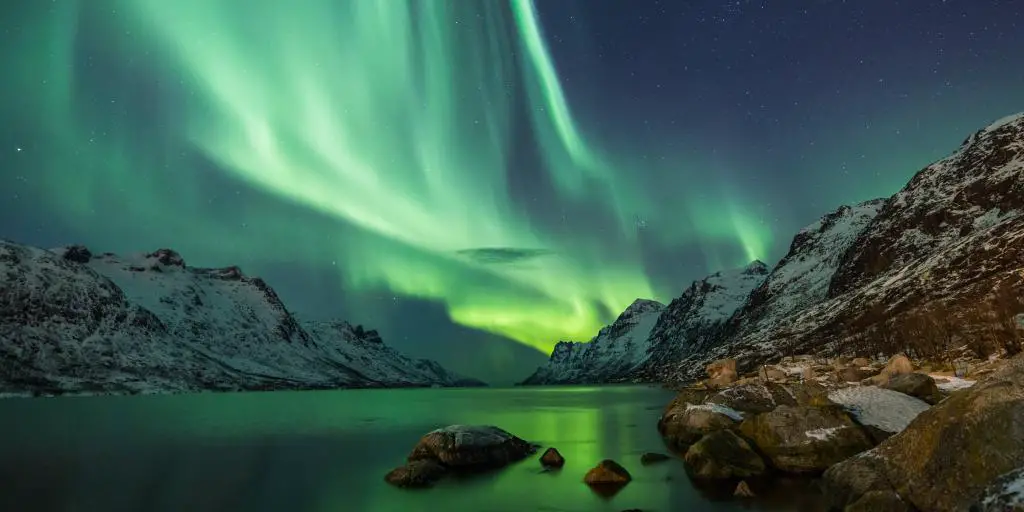 Aurora boreal verde sobre las montañas y el agua en Islandia. 