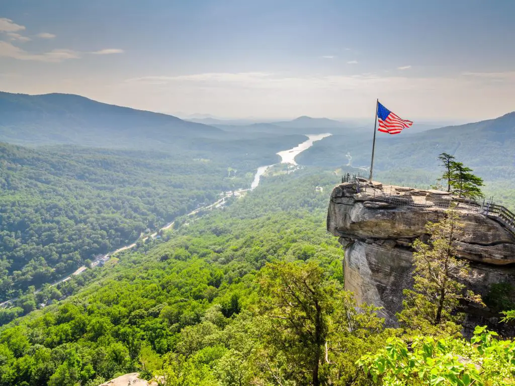 Chimney Rock en Chimney Rock State Park en Carolina del Norte, EE. UU. Con la bandera de EE. UU. En la parte superior de la roca sobre un valle de árboles y colinas.
