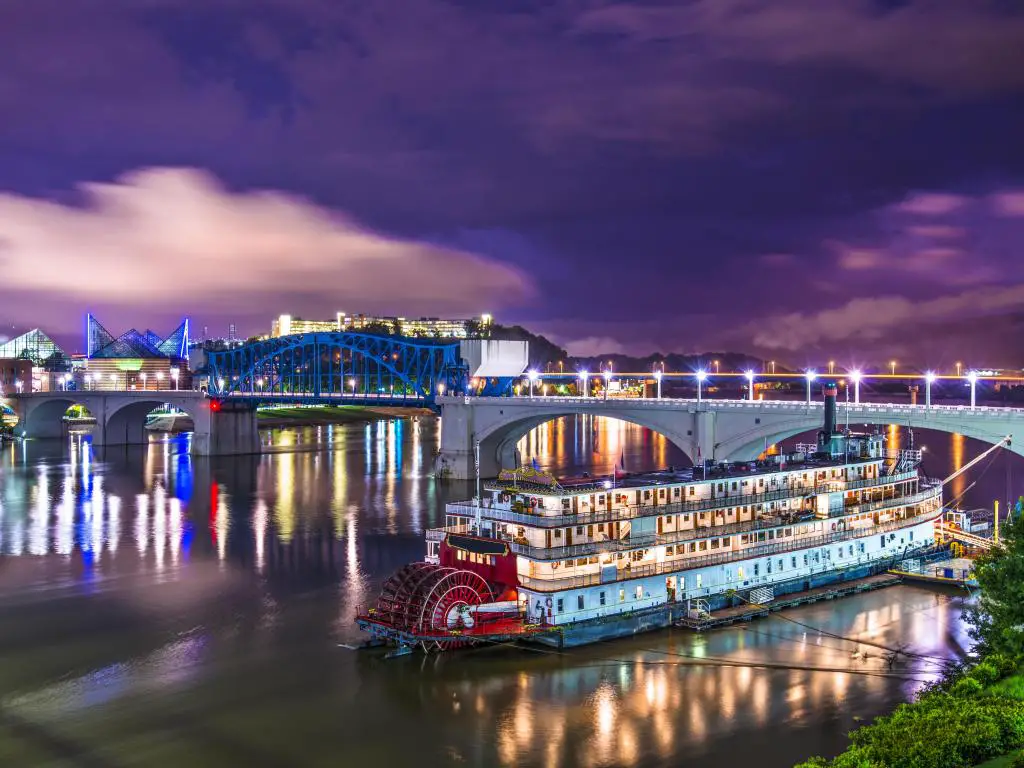 Chattanooga, Tennessee, EE.UU. en el centro de la ciudad sobre el río Tennessee con un gran barco en primer plano tomado por la noche.