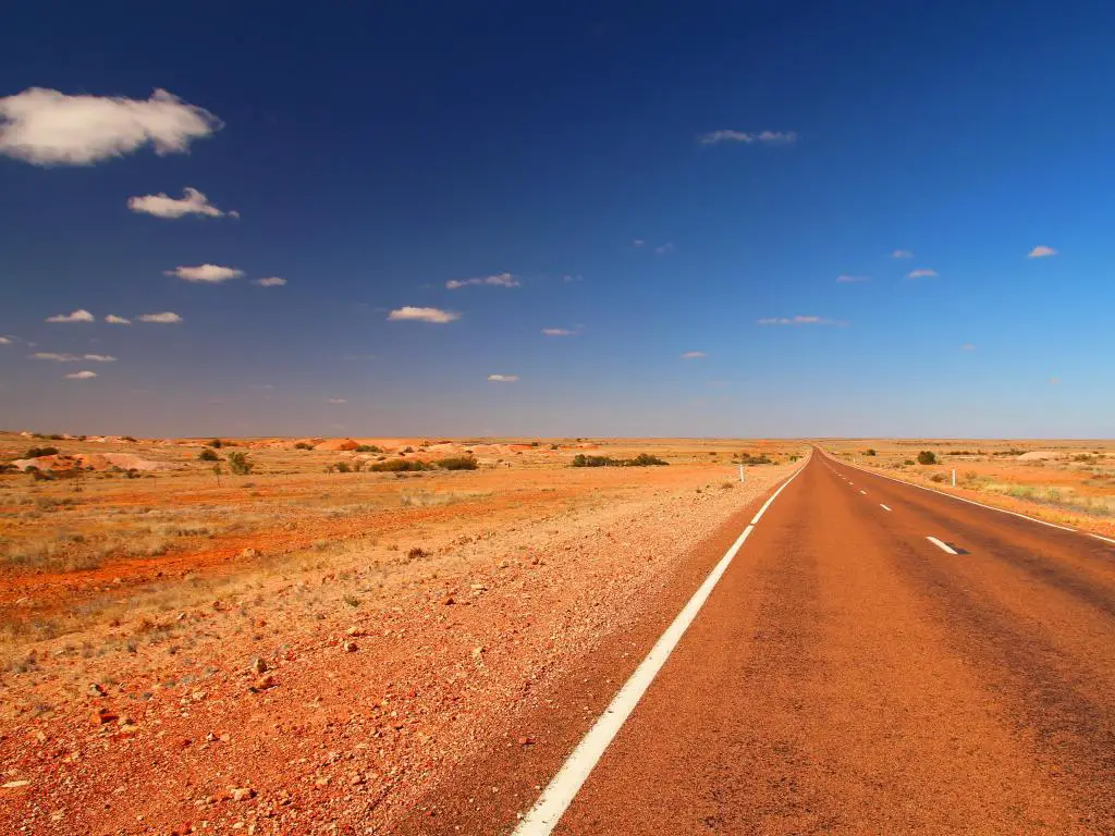 Stuart Highway, Australia Una vista de la autopista australiana a través del interior que muestra el desierto naranja en un día claro y soleado.