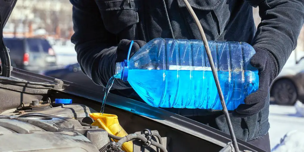 Una persona con guantes y abrigo vierte anticongelante en un sistema de refrigeración