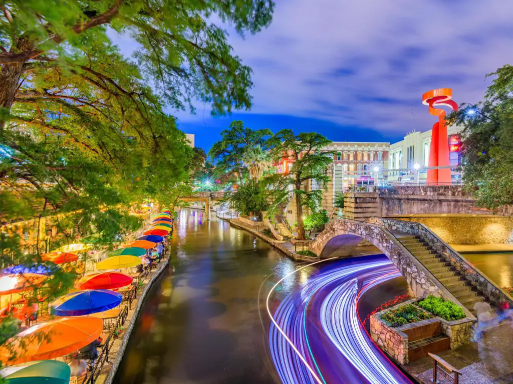 San Antonio, Texas, EE.UU. con el paisaje urbano en el River Walk tomado por la noche con coloridas sombrillas y árboles que sobresalen del río.