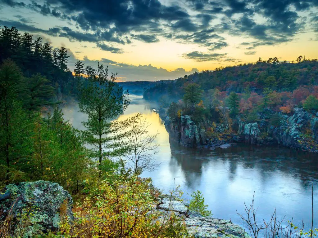 St Croix Falls, Wisconsin, EE.UU. con vistas al río al atardecer con árboles y rocas alrededor.