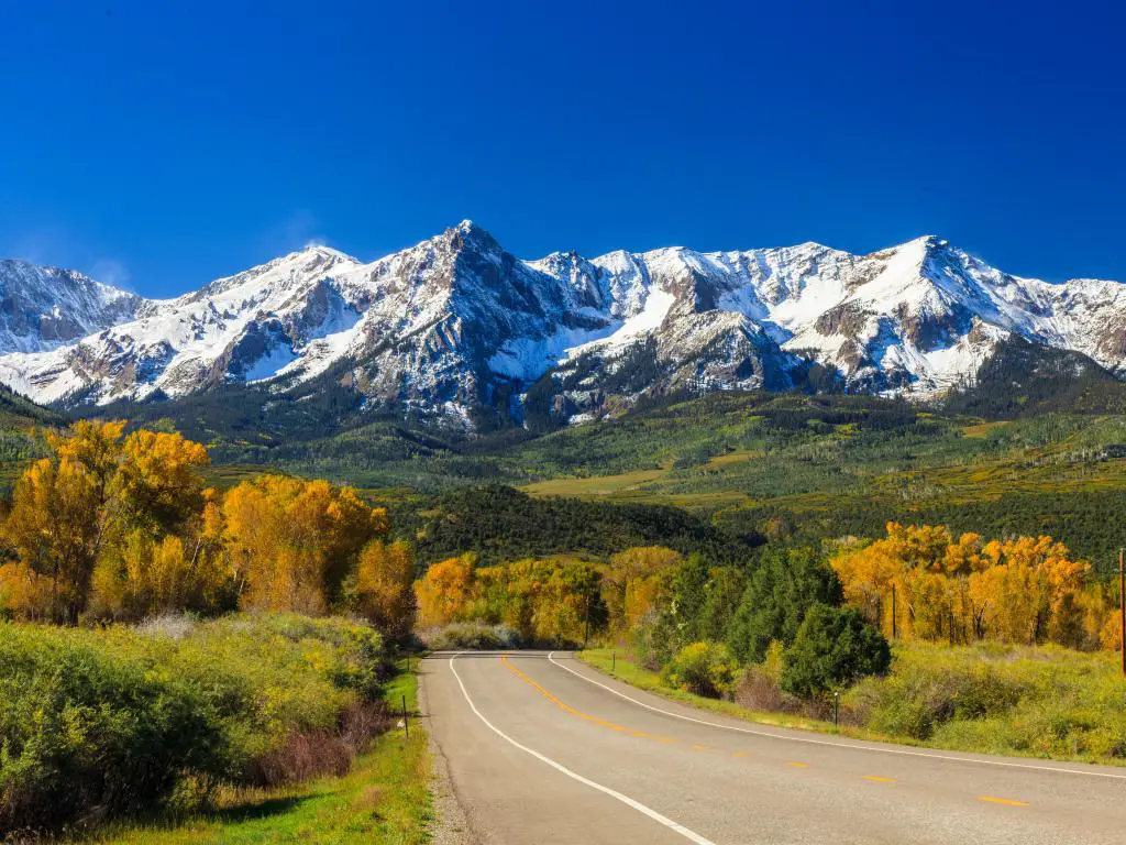 Camino rural con las Montañas Rocosas al fondo, temporada de otoño en Colorado