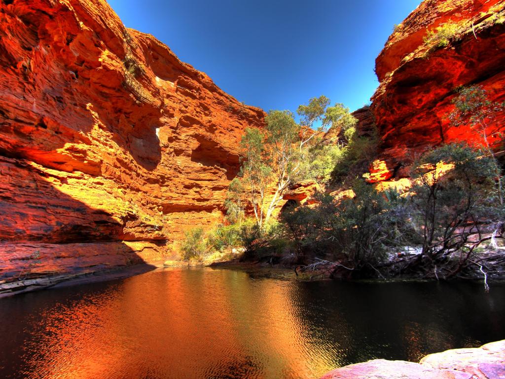 Sol brillando entre rocas rojas sobre el agua que corre a través de Kings Canyon, con cielo azul arriba