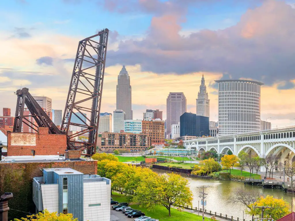 Cleveland, Ohio, EE.UU. con vistas al horizonte del centro al atardecer con el río y los árboles en primer plano. 