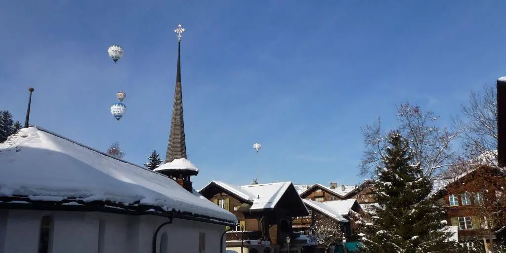 Globos aerostáticos despegando sobre la ciudad de Gstaad, Suiza, con la aguja de una iglesia en primer plano