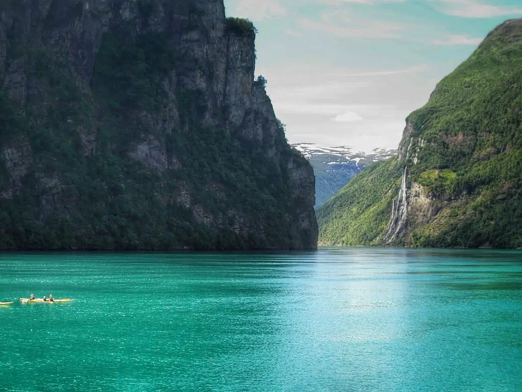 Los kayakistas reman en el fiordo turquesa noruego, con las cascadas Seven Sisters en la distancia