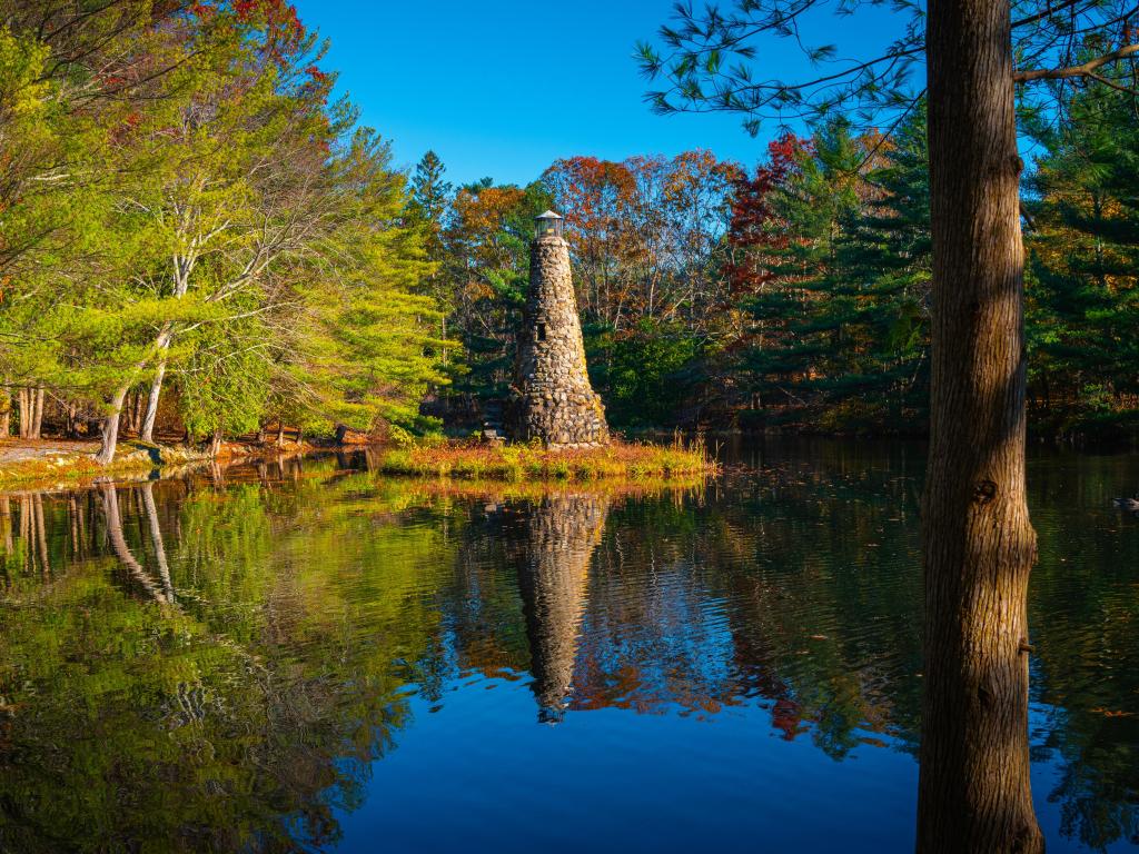 Duxbury Beach Park, Massachusetts, Estados Unidos, tomada en un lago tranquilo con bosque verde y faro en un día claro y soleado.