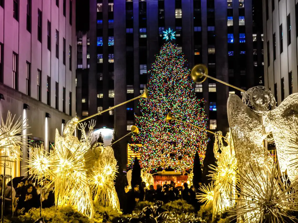Ángeles con gran árbol de Navidad con luz frente al centro Rockefeller.  Decoraciones famosas de Navidad en Midtown, Manhattan, en el centro de la ciudad de Nueva York.