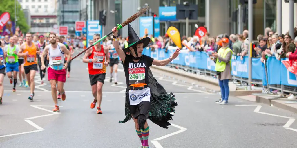 Corredor de maratón feliz vestido como una bruja siendo aclamado por el público 