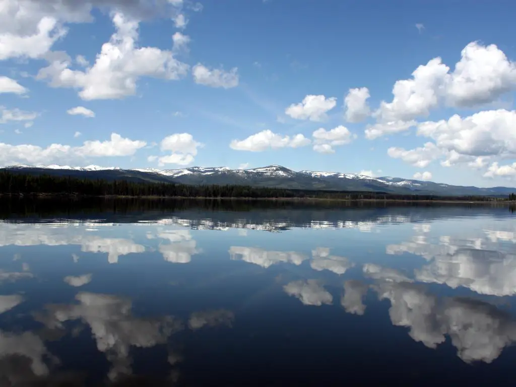 Seeley Lake, Montana, EE.UU. con reflejos de nubes en el lago tomados en un día soleado con montañas nevadas en la distancia.