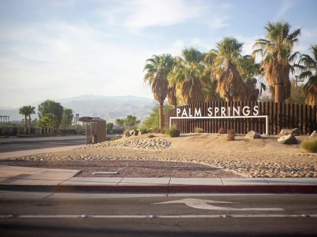 Ciudad de Palm Springs, California, EE.UU. en un día claro y soleado con el cartel y palmeras y un camino que conduce hacia las montañas. 