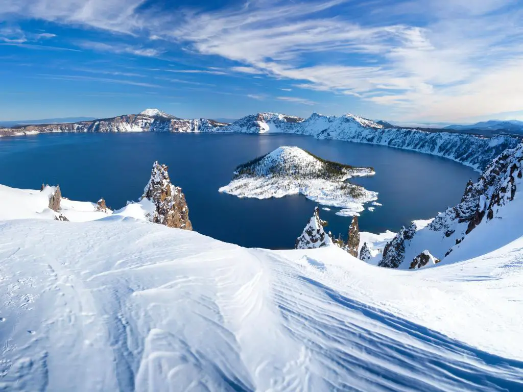 Vista del lago azul en el cráter del volcán con borde cubierto de nieve y laderas de montaña y cielo azul