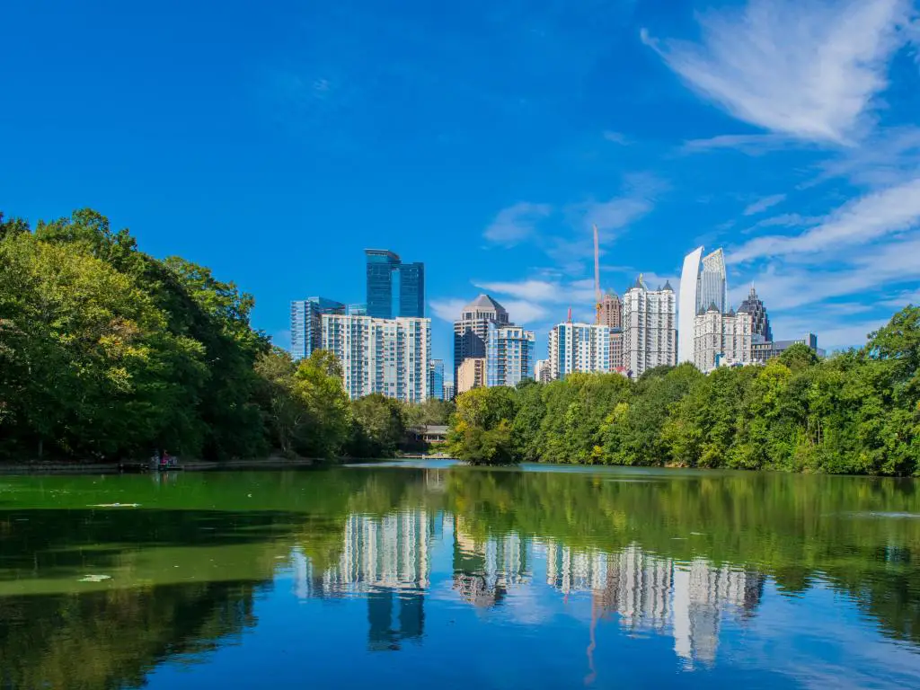 Atlanta, Georgia, EE.UU. con el horizonte de la ciudad al fondo en una tarde de verano y árboles que bordean el lago en primer plano.