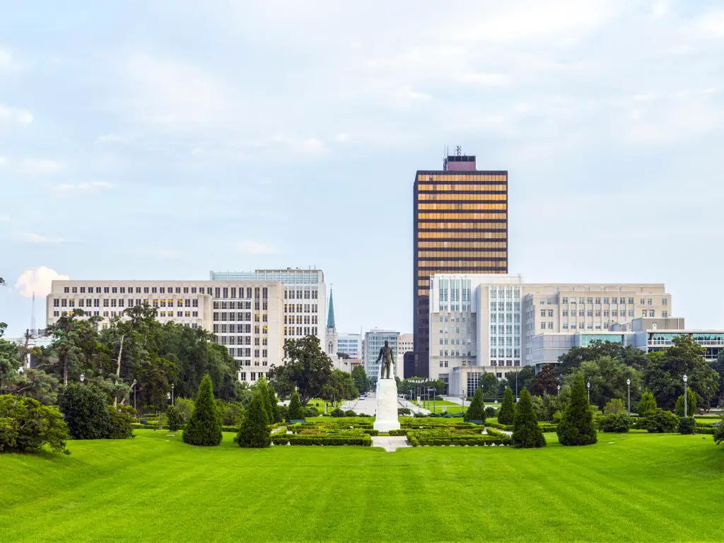 Baton Rouge, Luisiana, EE.UU. con el horizonte de la ciudad y la estatua de Huey Long en la distancia, parque verde en primer plano tomado en un día soleado.
