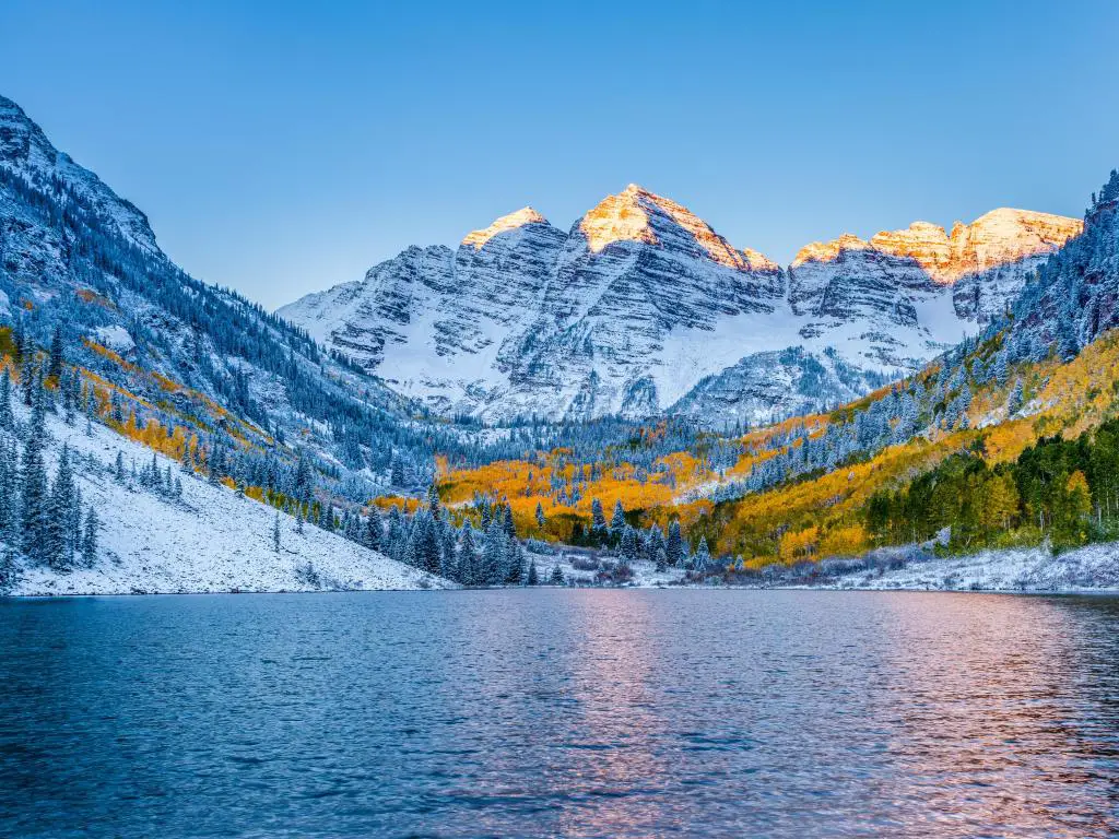 Aspen, Colorado, EE.UU. con Maroon Bells al amanecer en la distancia y un lago en primer plano tomado en invierno con nieve cubriendo la tierra.