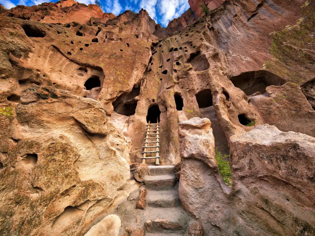 Monumento Nacional Bandelier, Nuevo México, EE.UU. con viviendas en los acantilados, una escalera y escalones que llegan a una puerta en los acantilados y se toman en un día soleado.