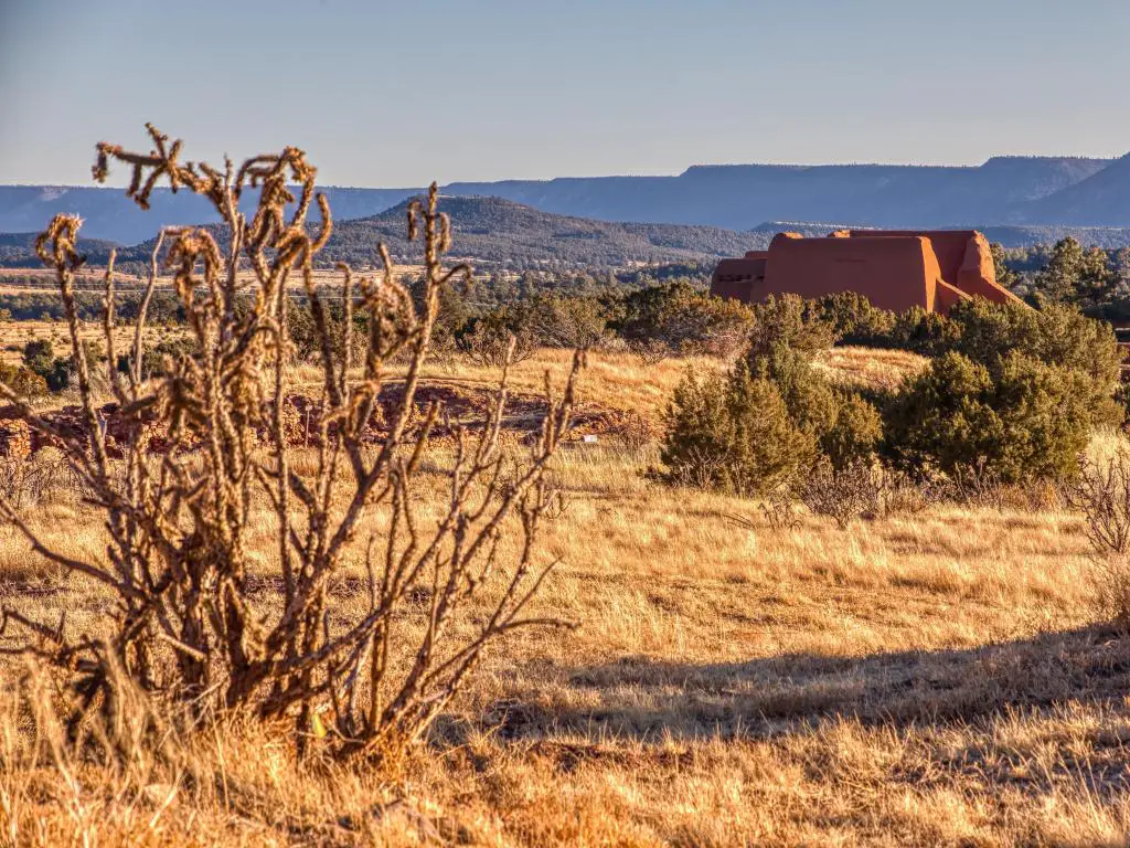 Parque Histórico Nacional de Pecos, Santa Fe, Nuevo México, EE.UU. con plantas, pastos y arbustos en primer plano y edificios y colinas en la distancia tomadas en un día soleado.