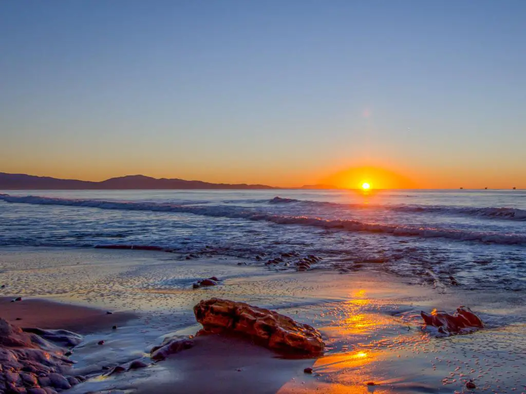 Santa Bárbara, California, EE.UU. tomada al amanecer con vistas a la playa, rocas en la arena y el mar a lo lejos.