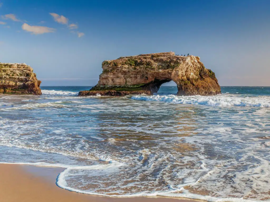 Santa Cruz, California, EE.UU. con los arcos en la playa estatal de Natural Bridges tomada en un día soleado con una playa de arena en primer plano.