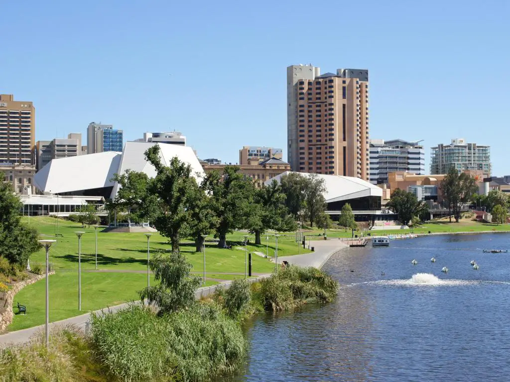 Adelaida, Australia, con un panorama de la ciudad en un día soleado con el río en primer plano y los edificios al fondo.