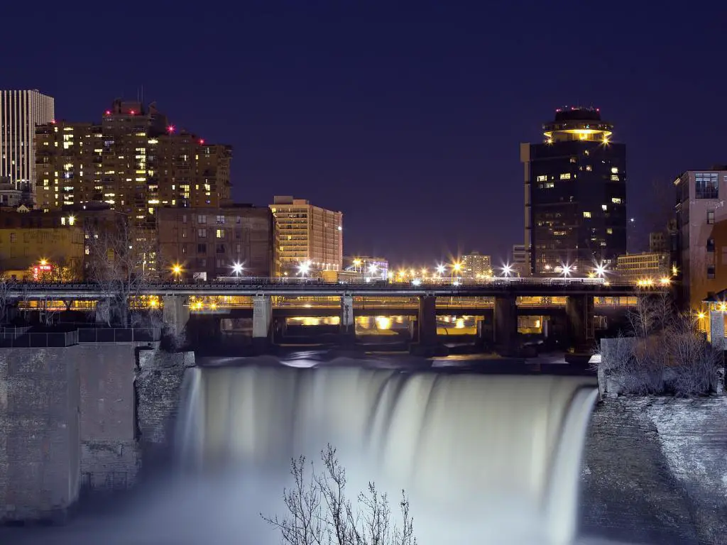 Rochester, Nueva York, Estados Unidos, con el horizonte nocturno de los rascacielos de la ciudad al fondo y la cascada en primer plano.