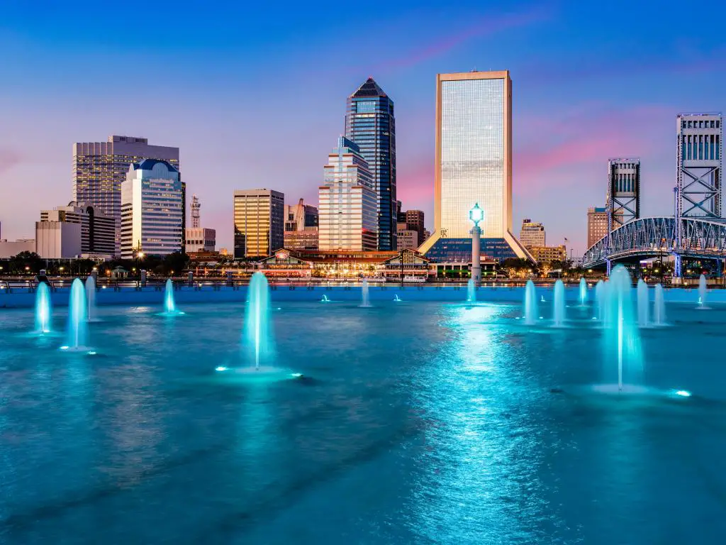 Jacksonville, Florida, EE.UU. con el horizonte de la ciudad al fondo y la fuente iluminada por la noche en primer plano.